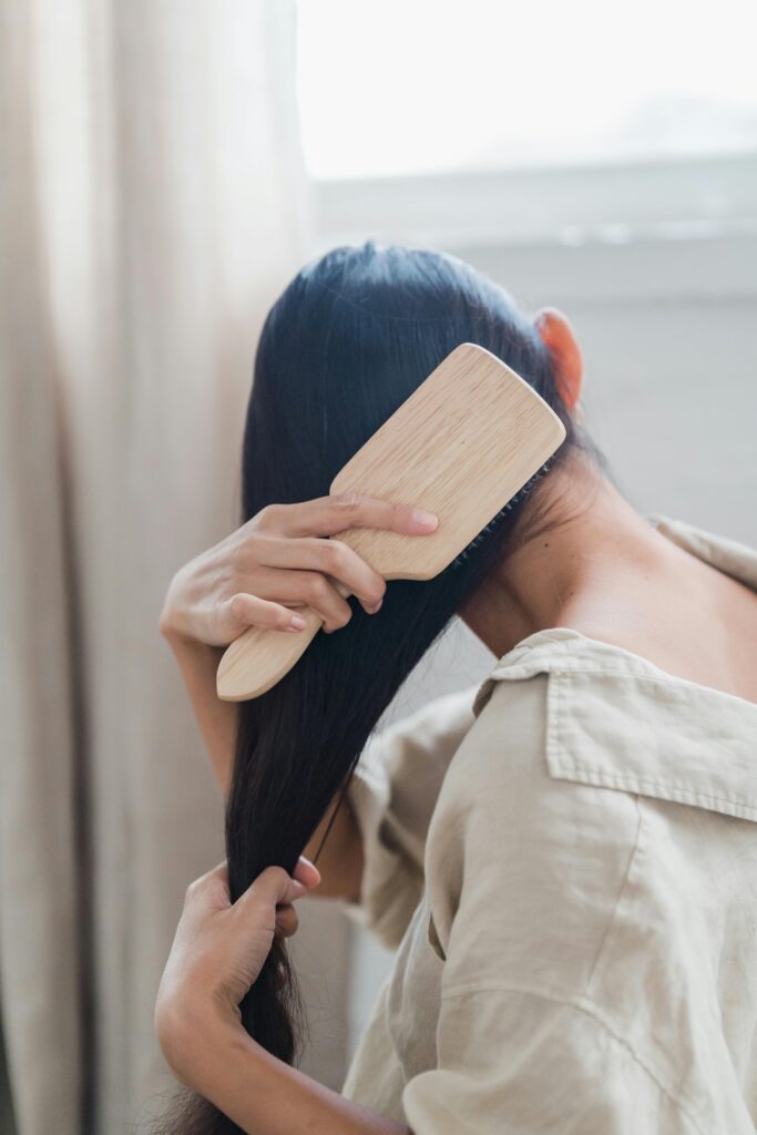 Na imagem há uma mulher penteando seu cabelo liso, e o tema do nosso post é exatamente isso " Cuidados essenciais para cabelos lisos"