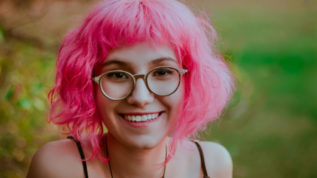 Na imagem tem uma adolescente de óculos com os seus cabelos soltos e pintado de rosa, onde retrata o tema " Cabelos Maluco Infantil"