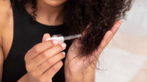 Mulher aplicando um produto em seu cabelo, onde representa o tema: Couro cabeludo seco causas e soluções que funcionam