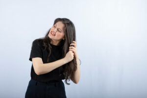 Mulher tocando em seu cabelo, onde representa o tema: Couro cabeludo seco causas e soluções que funcionam