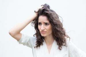 Mulher com a mão no cabelo com as de preocupada, representando o tema oleosidade no couro cabeludo