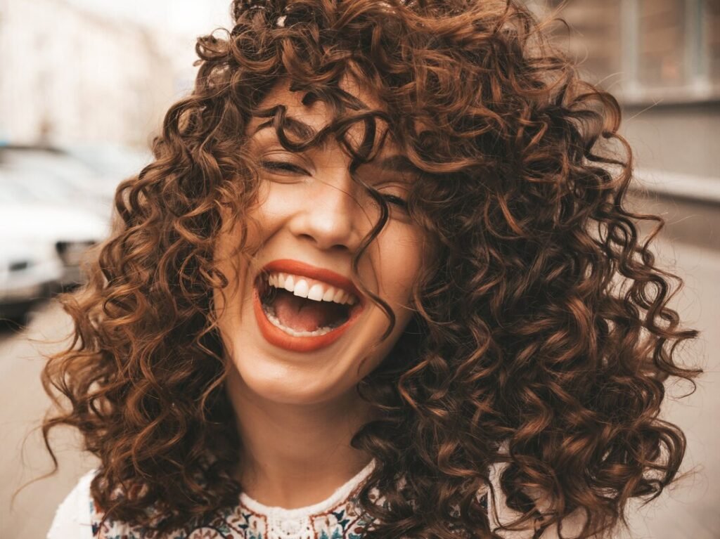 Mulher feliz com um lindo cabelo cacheado solto e bem definido, onde representa o tema: Melhores Produtos para cabelos cacheados 2025